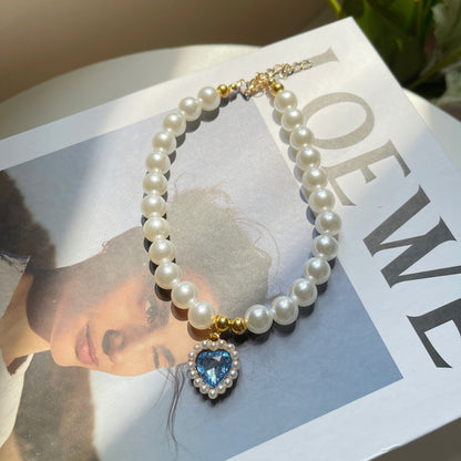 Pearl necklace with a heart-shaped blue gemstone pendant on a magazine page.